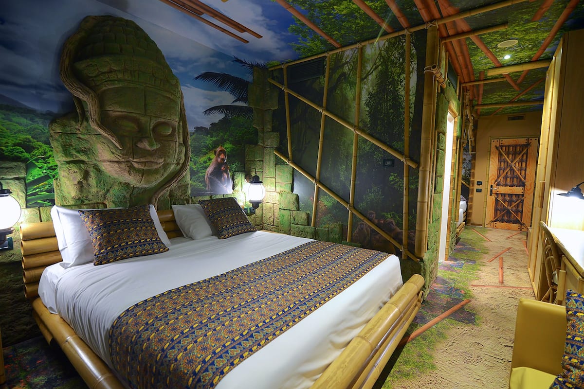 Una habitación con una cama grande, una escultura de cabeza de piedra y un mural con una escena selvática.