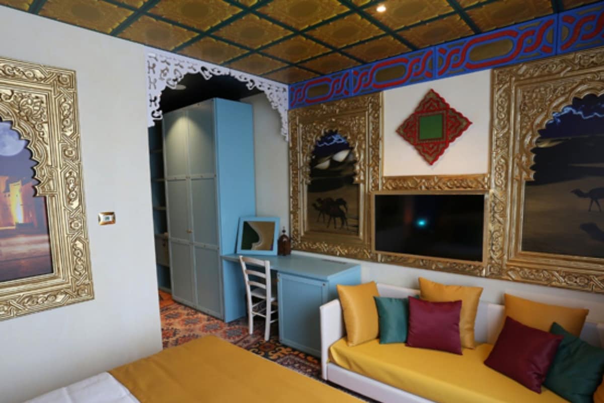 Une pièce comprenant un lit, un canapé agrémenté de coussins colorés, un bureau avec une chaise et une grande fenêtre.