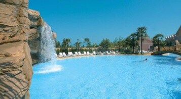 Una piscina con una cascata, circondata da poltroncine a sdraio e palme.