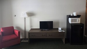 Habitación de hotel con un sillón rojo, un escritorio con televisor, una lámpara, microondas y refrigerador.