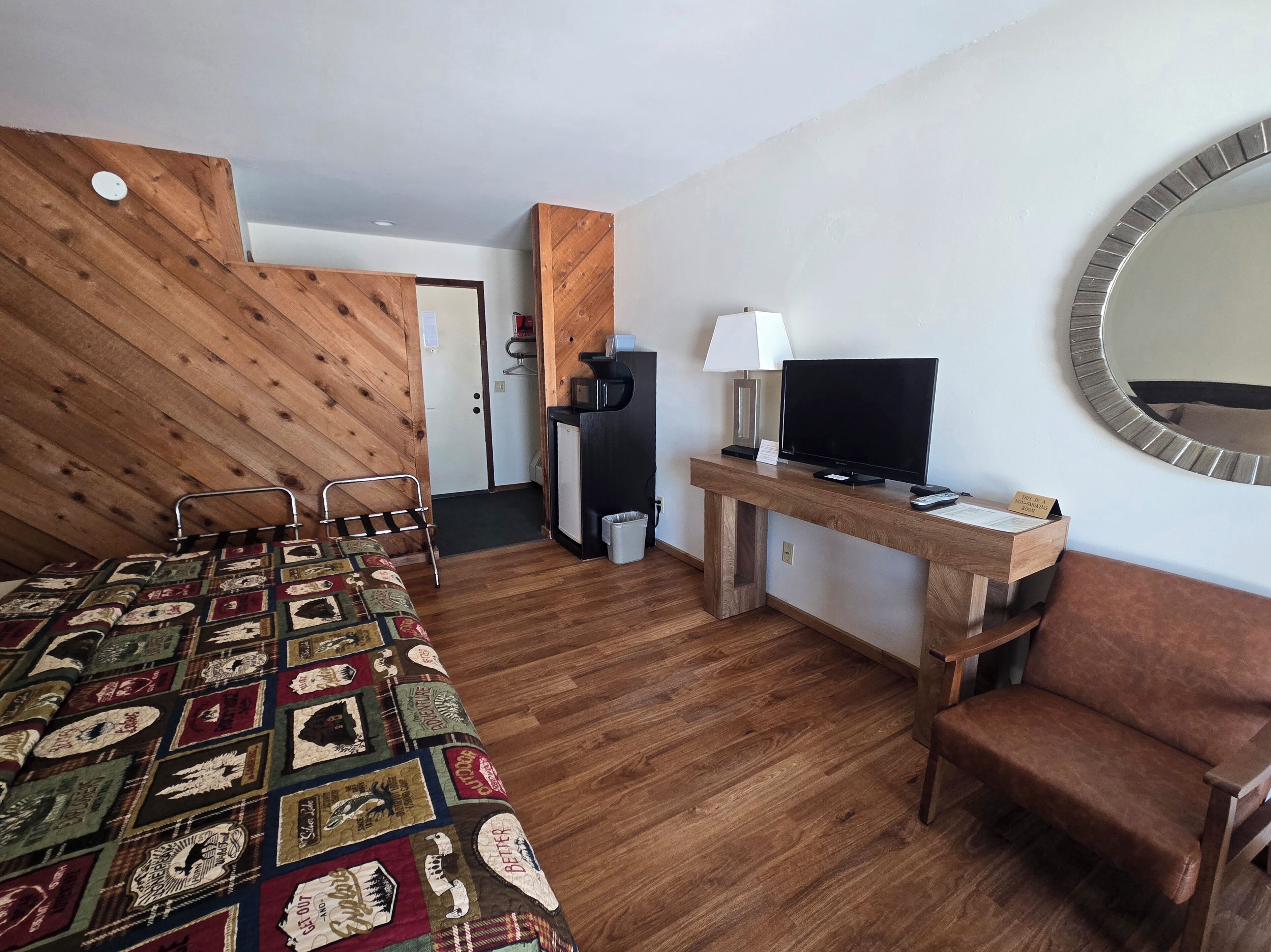 A hotel room with a wooden bed, a desk with a TV, a chair, and a mirror on the wall.