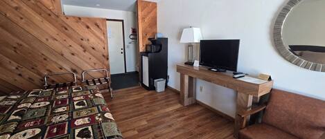 A hotel room with a wooden bed, a desk with a TV, a chair, and a mirror on the wall.