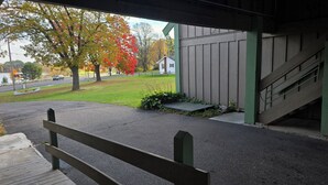 Un espacio al aire libre techado con un banco de madera, una escalera y vistas a un área verde con árboles y un edificio al fondo.