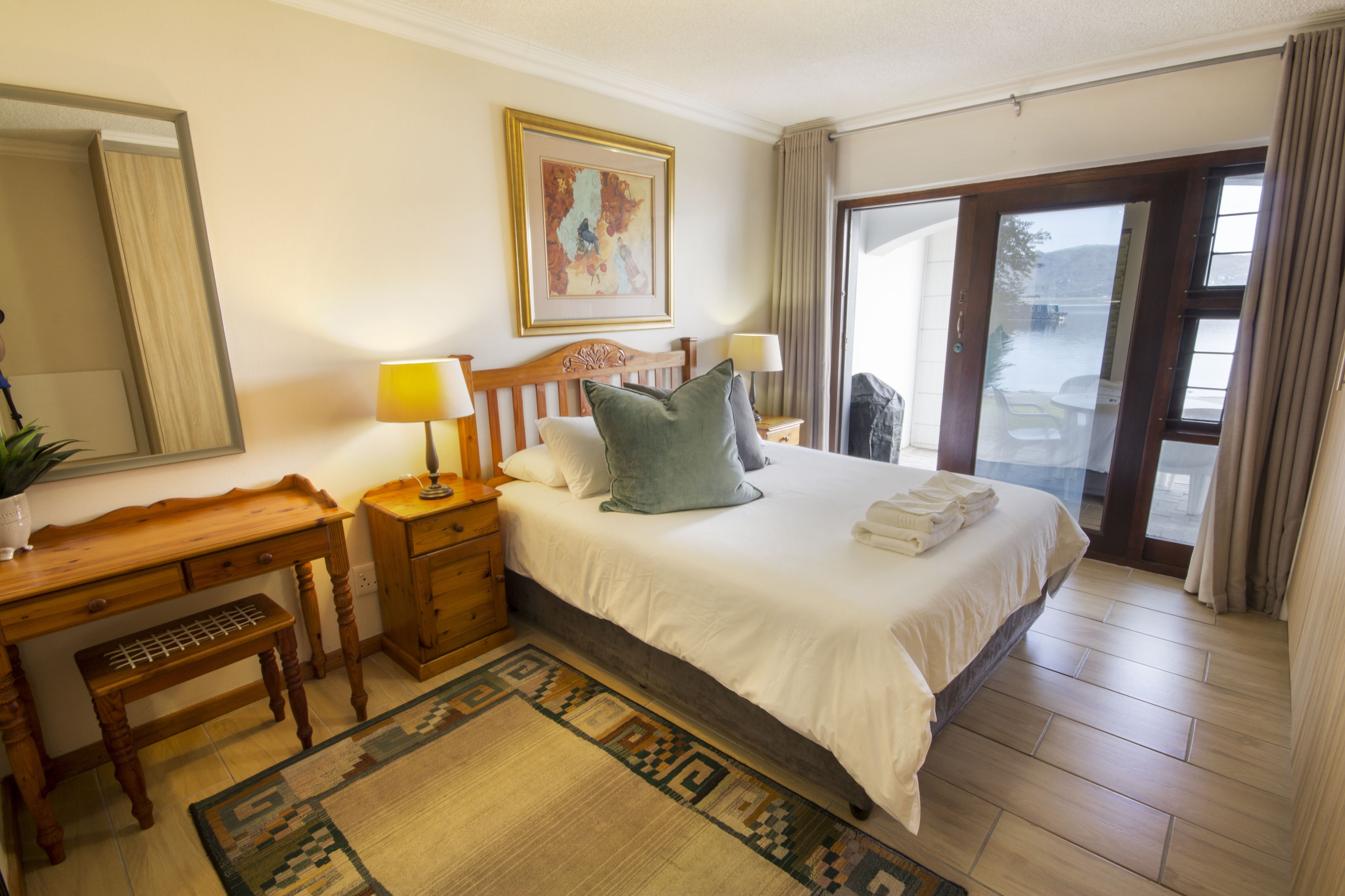 A hotel room with a large bed, wooden desk, and a view through a glass door.