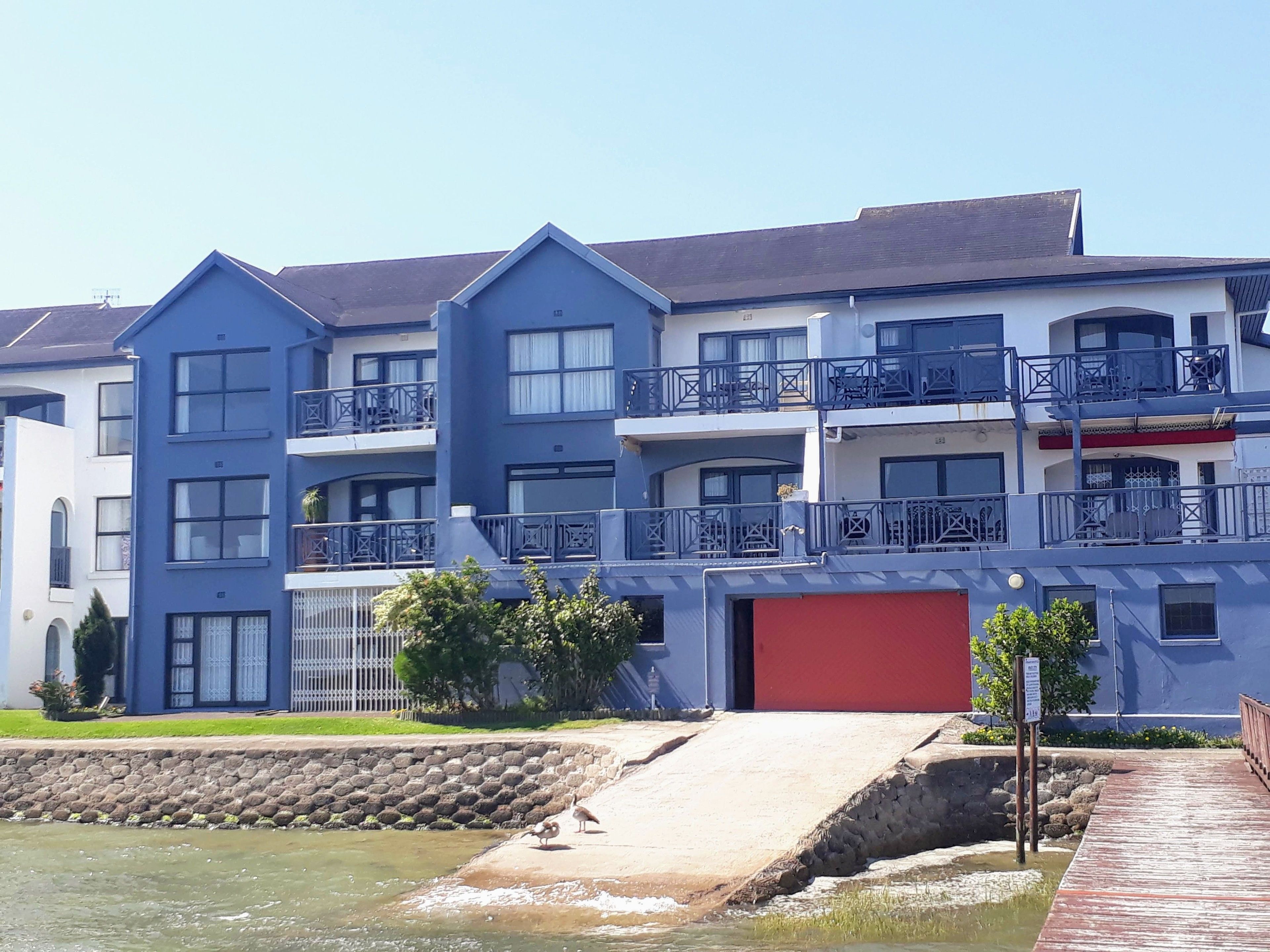 A multi-story residential building with balconies, a red garage, and a waterfront view.