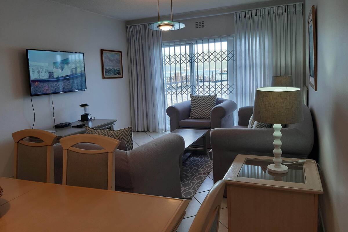 A living room with a TV, sofa, chairs, a table, and a lamp.