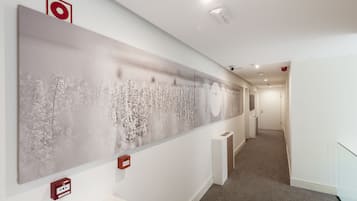 Un pasillo con un cuadro abstracto grande en la pared, un detector de incendios y una rejilla de ventilación.