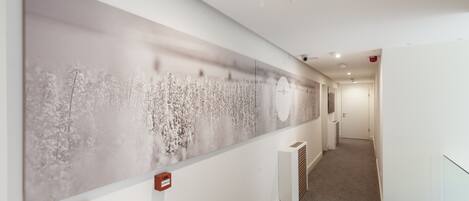 A hallway with a large abstract painting on the wall, a fire alarm, and a vent.