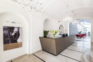 Un moderno vestíbulo de hotel con mostrador de recepción, candelabros y un cartel grande en la pared.