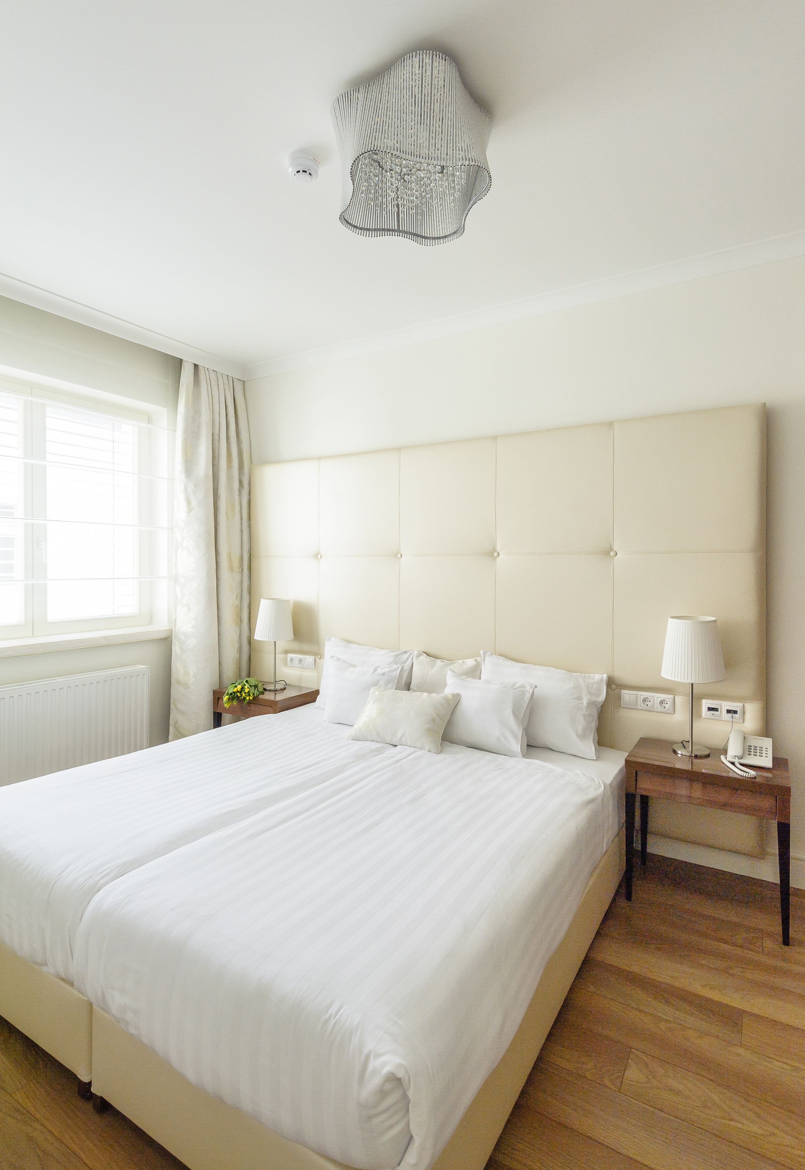A large bed with white linens, a wooden nightstand with a lamp, and a ceiling light fixture.