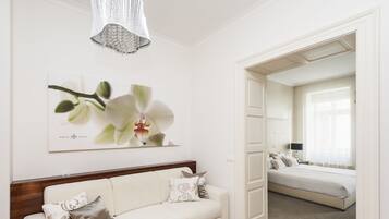 A hotel room with a white sofa, a bed, a chandelier, and a framed orchid artwork.