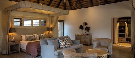A room with a bed, a sofa, a chair, a small table, and a decorative wall piece.