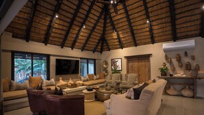 A spacious living room with a high thatched ceiling, a large flat-screen TV, and a variety of seating options including sofas and armchairs. - Inyati Game Lodge (Sabi Sand Reserve)