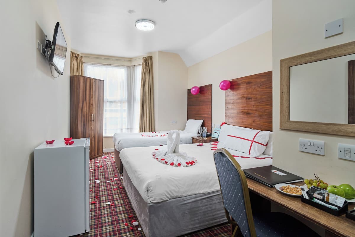 Quarto de hotel com duas camas, uma escrivaninha, um frigorífico e um espelho.