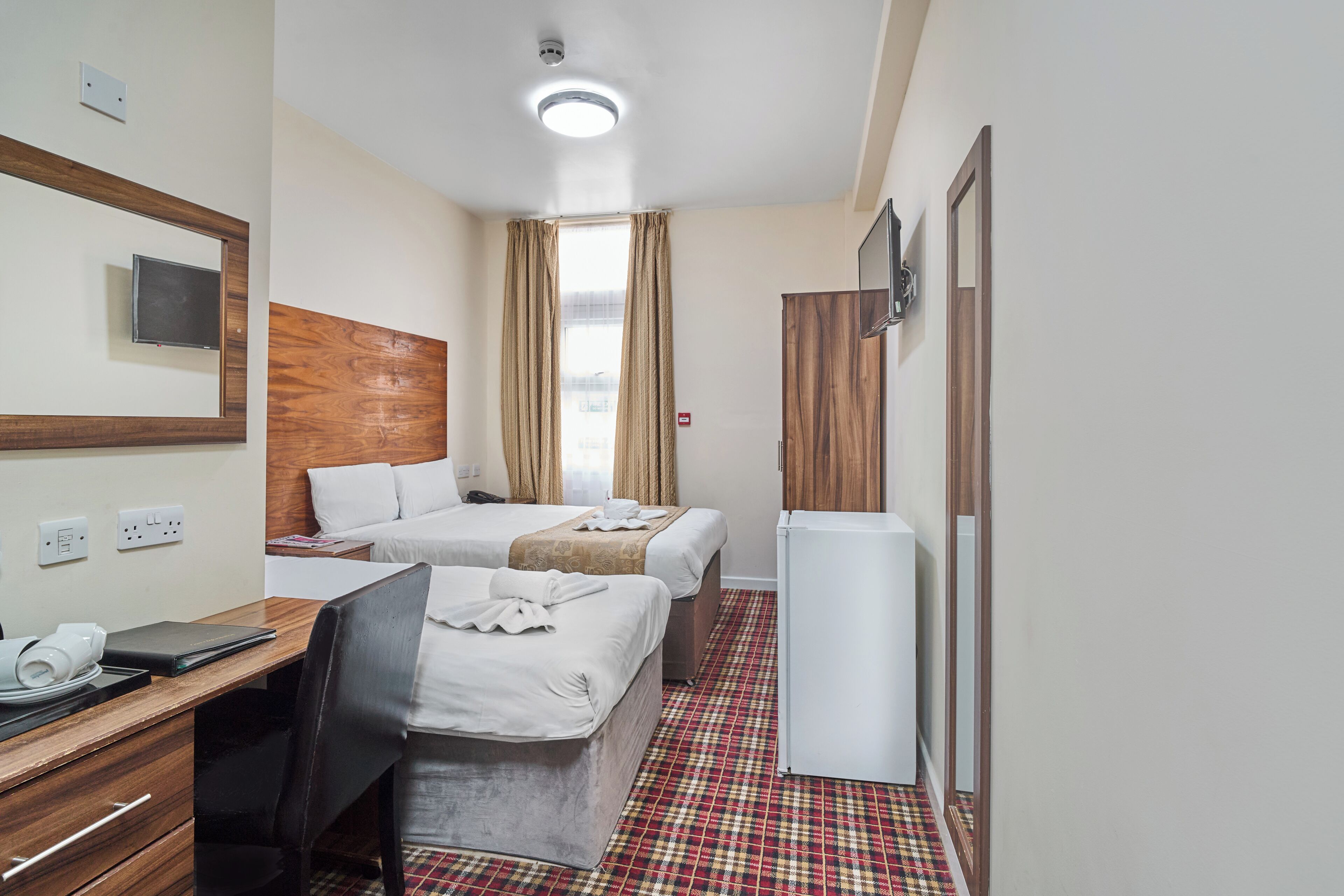 A hotel room with two beds, a desk, a chair, a television, and a refrigerator.