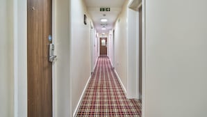 Un pasillo de hotel con alfombra a cuadros, puertas a ambos lados y un letrero de salida de incendios en el techo.