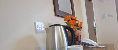 Zona de recepción de un hotel, con un mostrador de madera, una cafetera, tazas, un teléfono y un jarrón con flores.