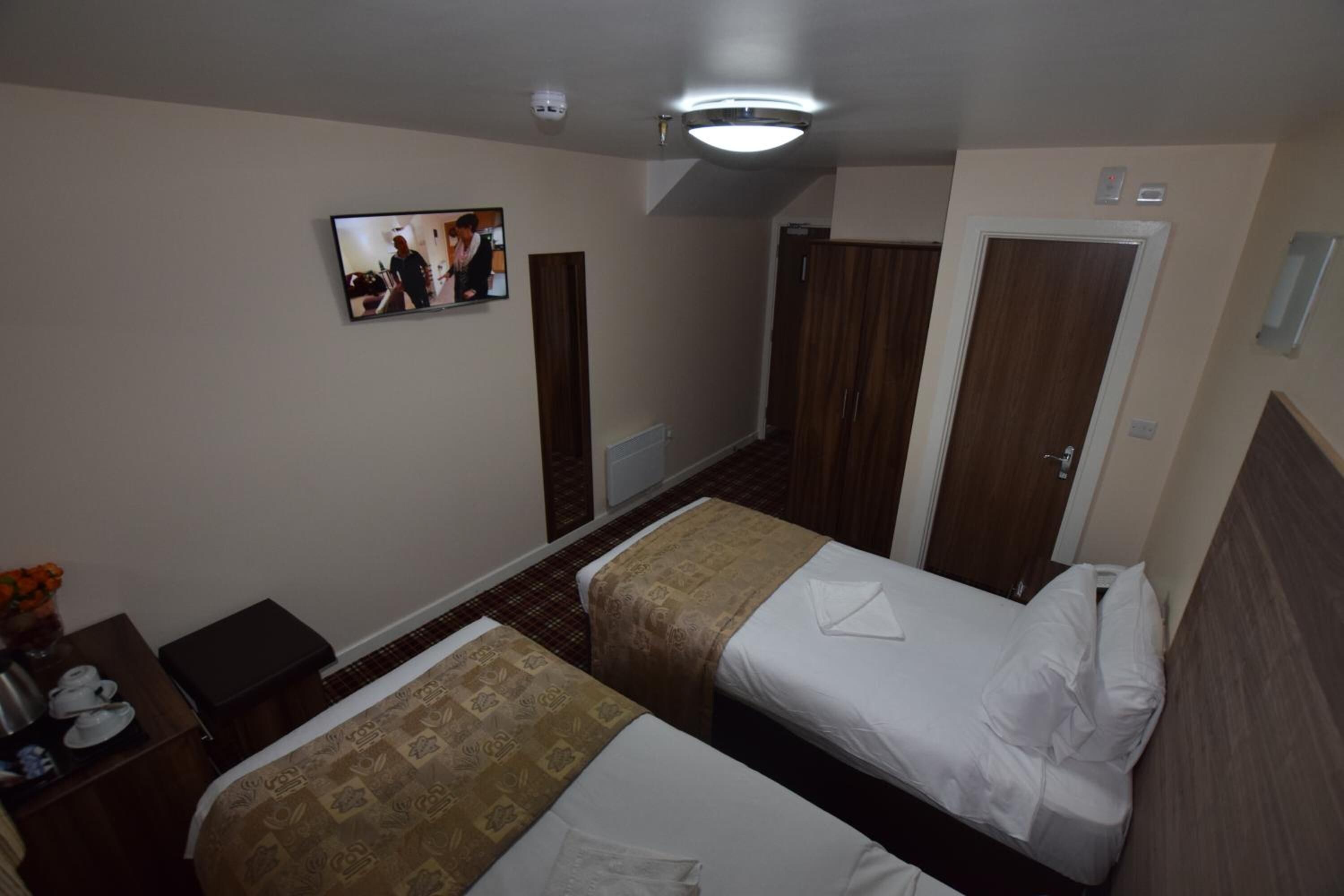 A hotel room with two beds, a TV on the wall, a desk with a vase of flowers, and a wardrobe.