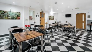 Un comedor de hotel con suelo de cuadros, varias mesas y sillas, y obras de arte en las paredes.
