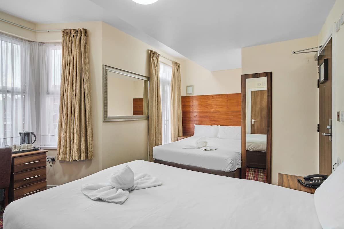 Quarto de hotel com duas camas, uma escrivaninha, uma cadeira, um telefone e um espelho.