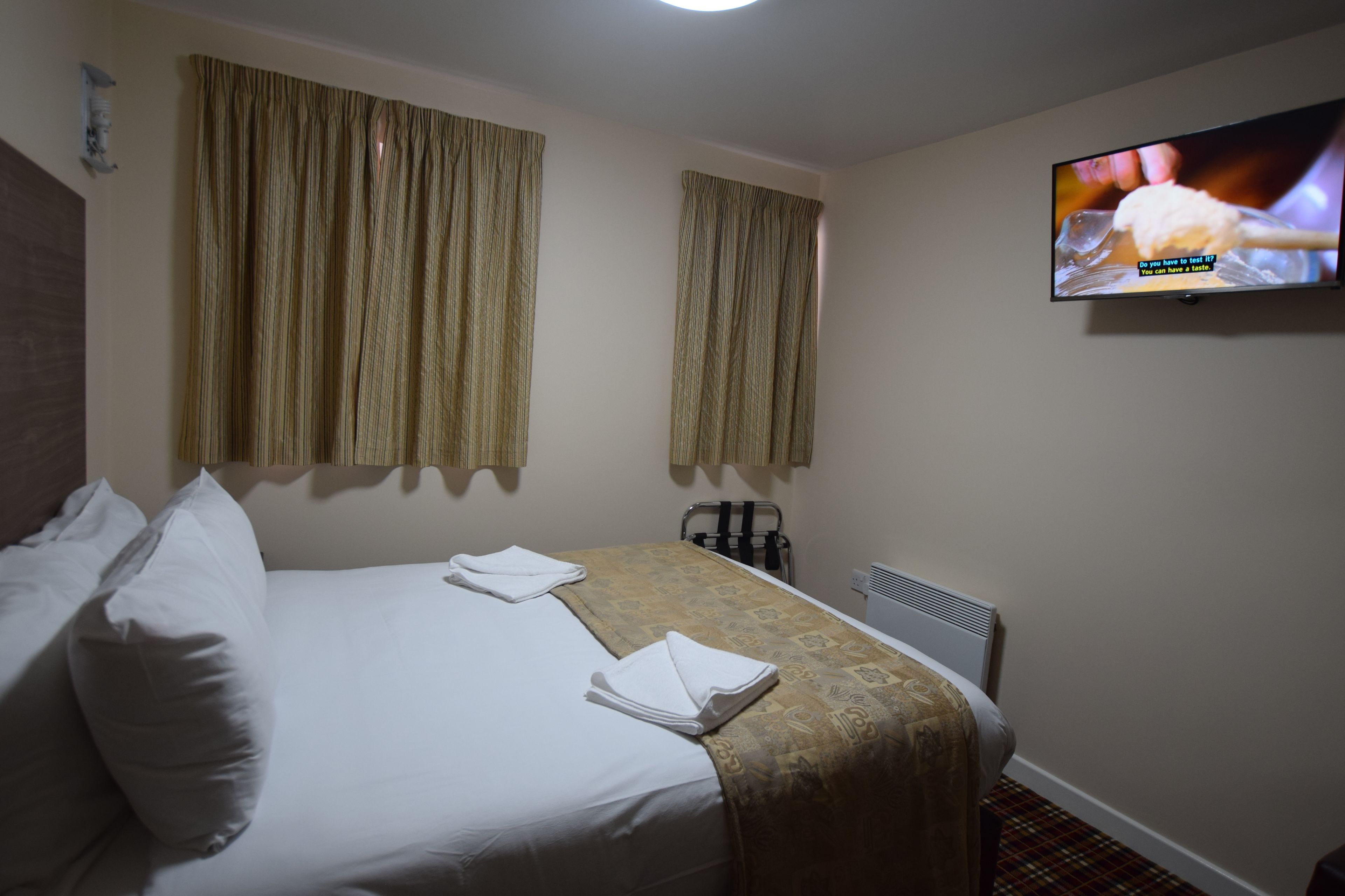 A hotel room with a bed, two curtains, a television, and a radiator.
