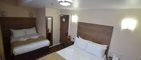 Una habitación de hotel con dos camas, una mesita de noche con teléfono y una lámpara de pared.