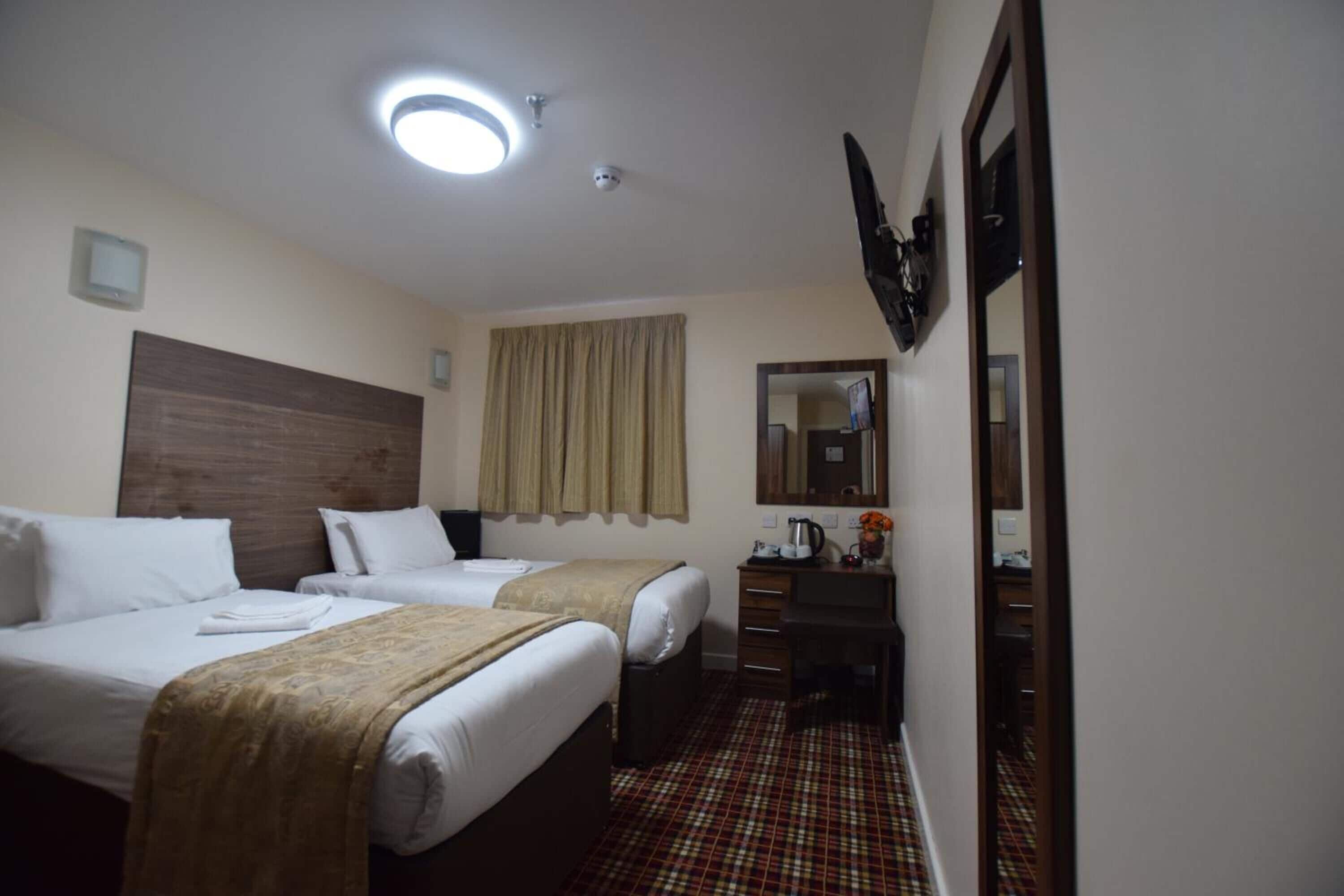 Een hotelkamer met twee bedden, een bureau, een spiegel en een raam met gordijnen.