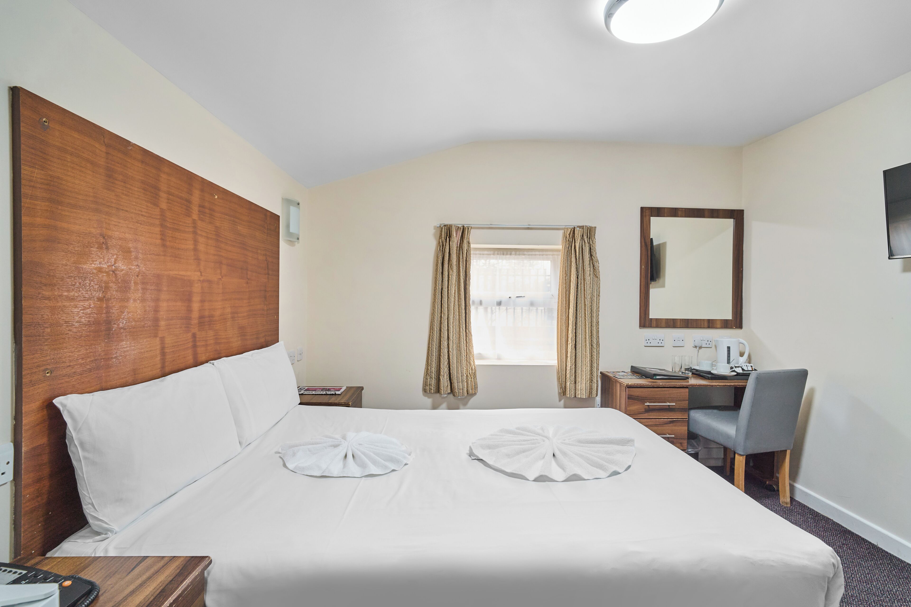 A hotel room with a bed, a desk, a chair, a television, and a window with curtains.