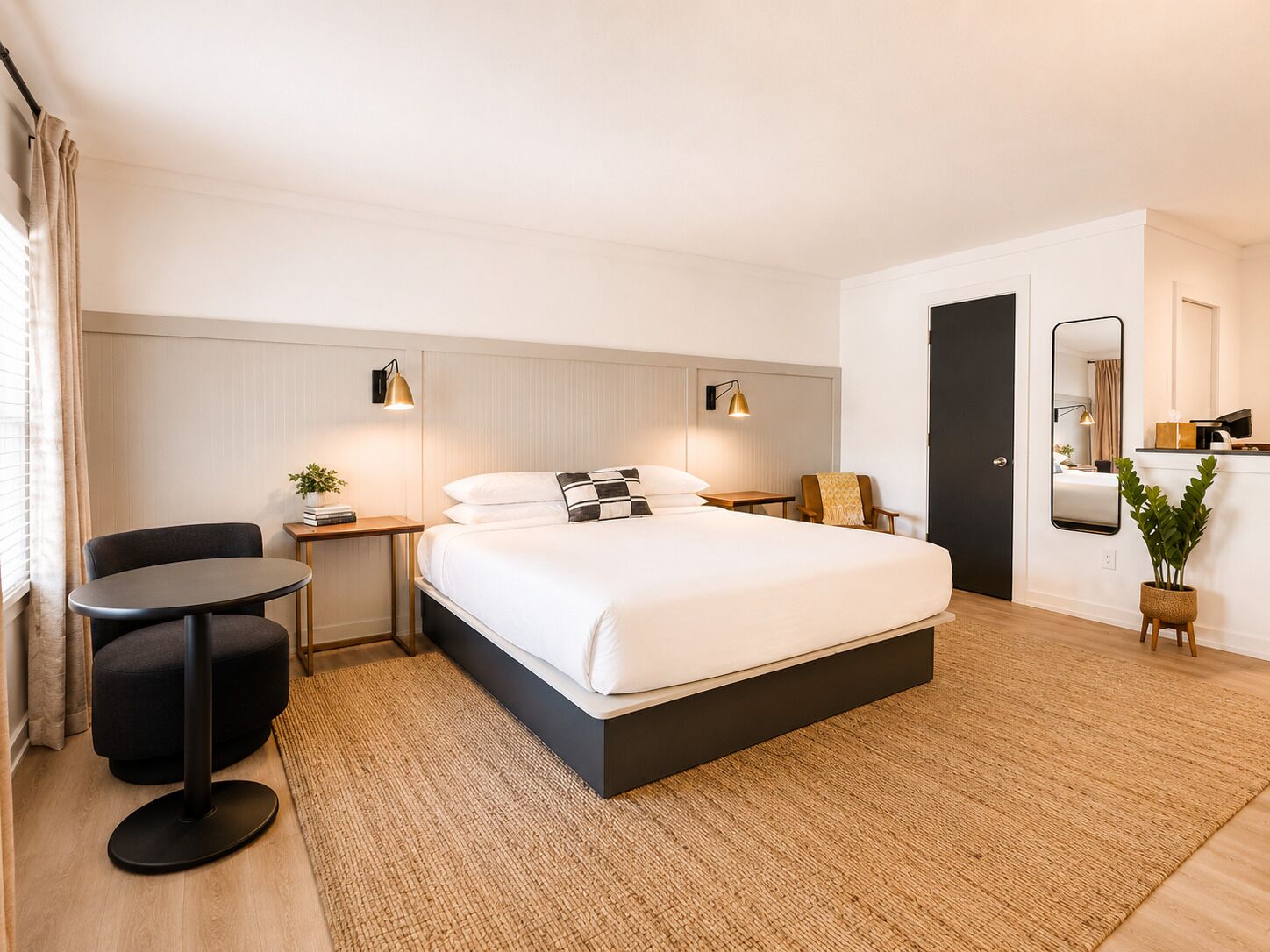 Une chambre d’hôtel moderne avec un grand lit, une petite table ronde, une chaise, un bureau et un miroir.