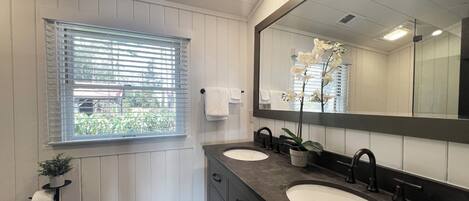 Un baño con dos lavamanos, un espejo grande y una ventana con persianas.