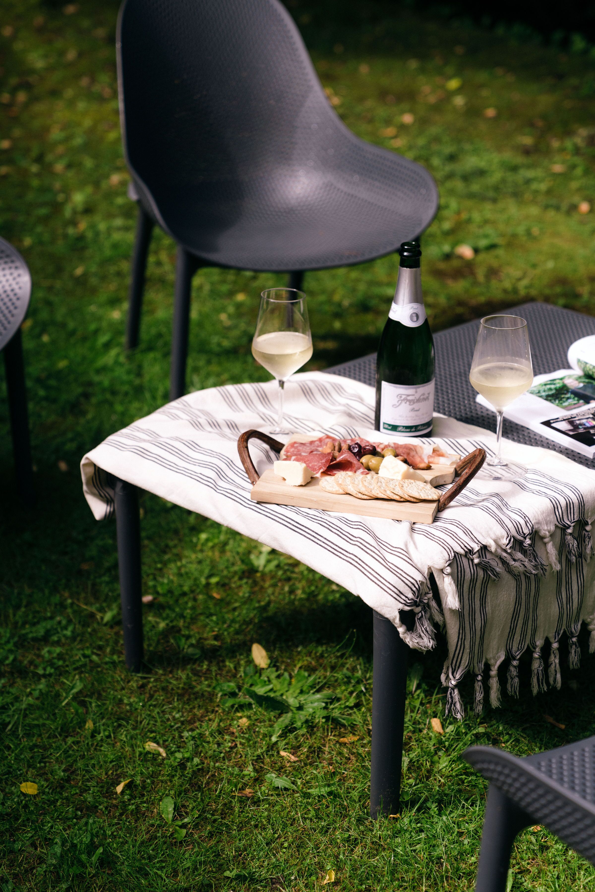 A table set outdoors with a bottle of wine, glasses, and a charcuterie board.