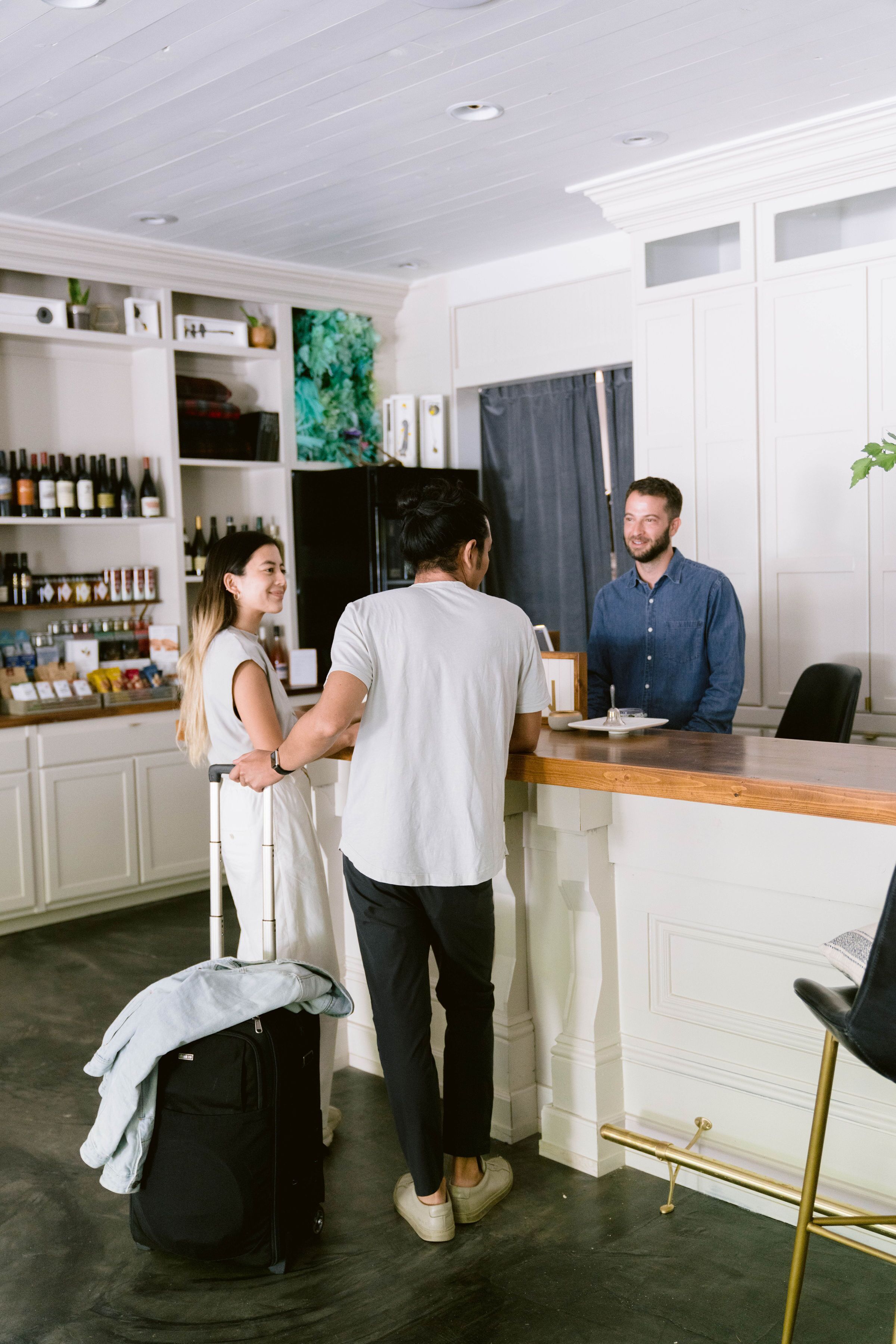 Uma área de bar com balcão, prateleiras com garrafas e uma pessoa em pé no balcão.