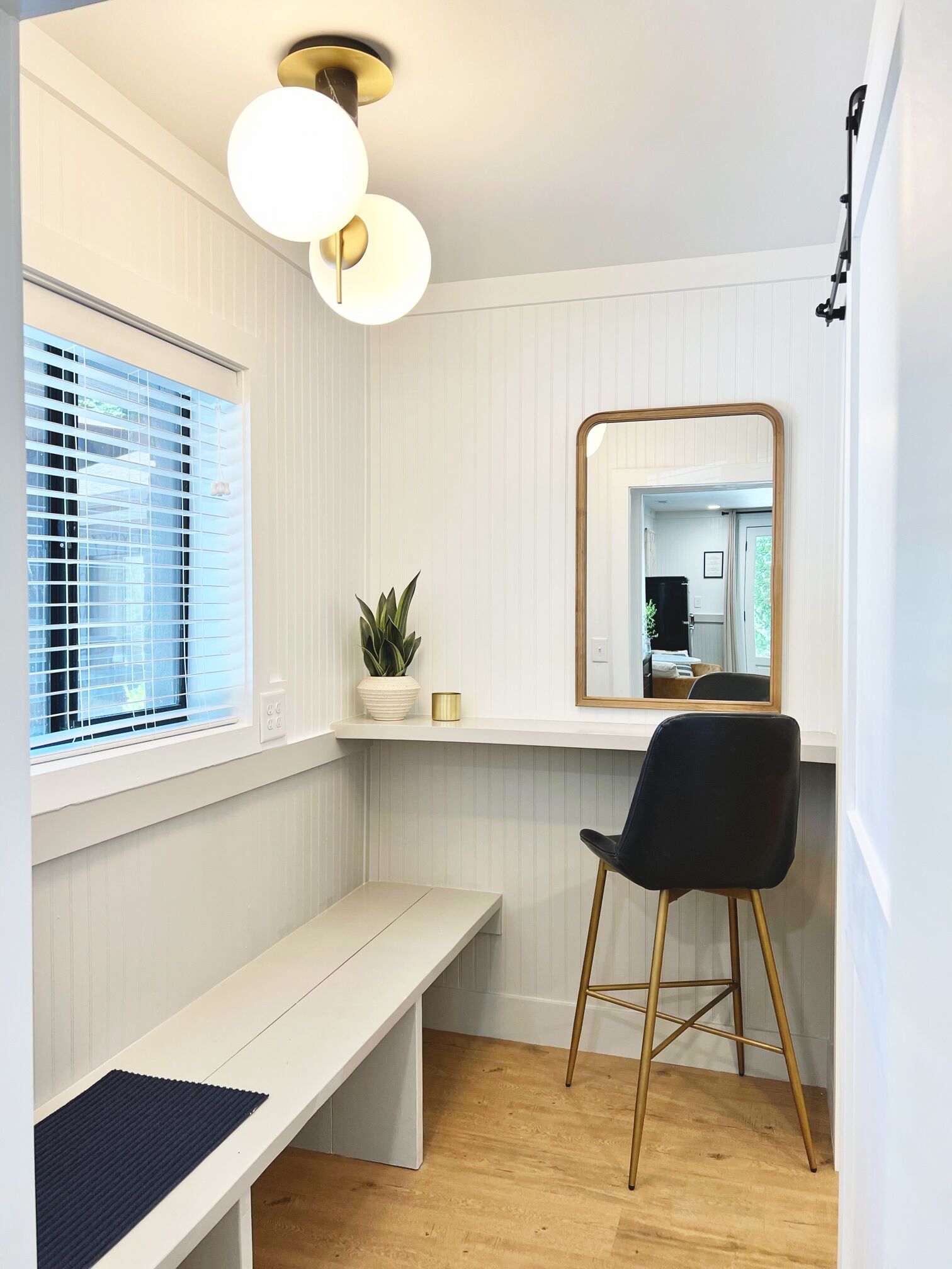 A room with a white bench, a black chair, a mirror, and a potted plant.