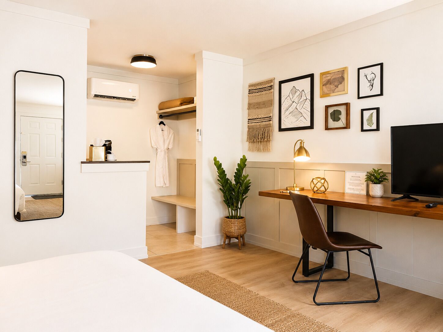 A modern hotel room with a wooden desk, a TV, a mirror, a robe, and a small plant.
