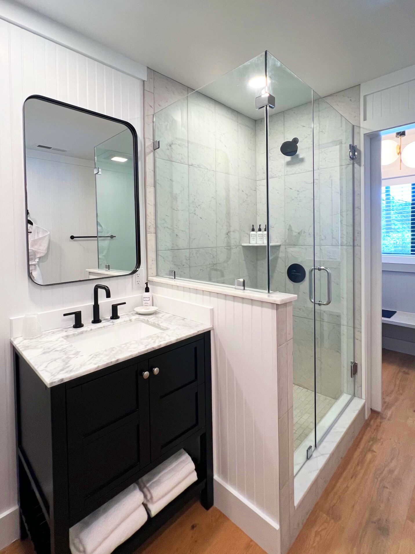 A modern bathroom with a white vanity, black cabinets, a glass shower enclosure, and a large mirror.