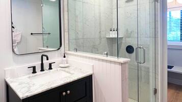 A modern bathroom with a white vanity, black cabinets, a glass shower enclosure, and a large mirror.