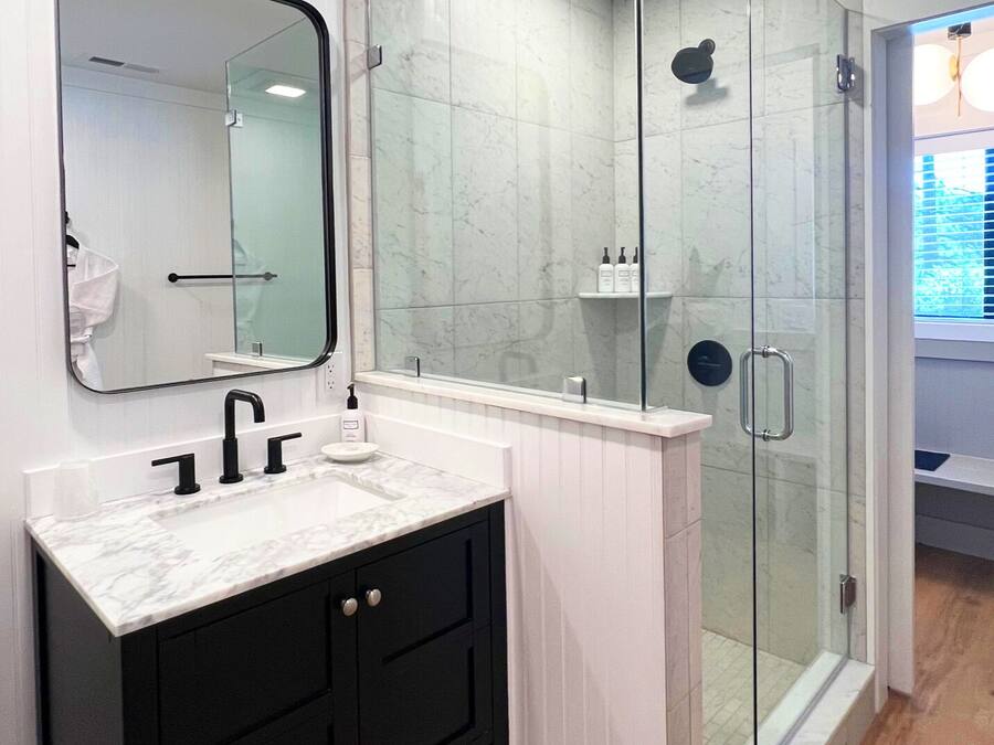 A modern bathroom with a white vanity, black cabinets, a glass shower enclosure, and a large mirror.