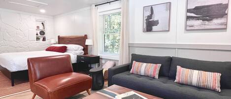 Una habitación de hotel moderna con cama, un sillón de cuero, sofá, mesa de centro y obras de arte en las paredes.