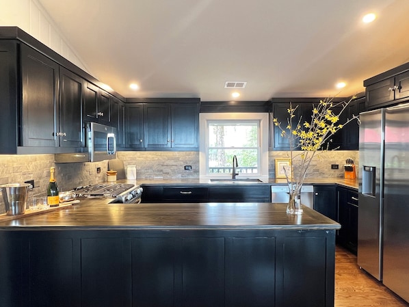 A modern kitchen with dark cabinetry, a central island, stainless steel appliances, and a window providing natural light.