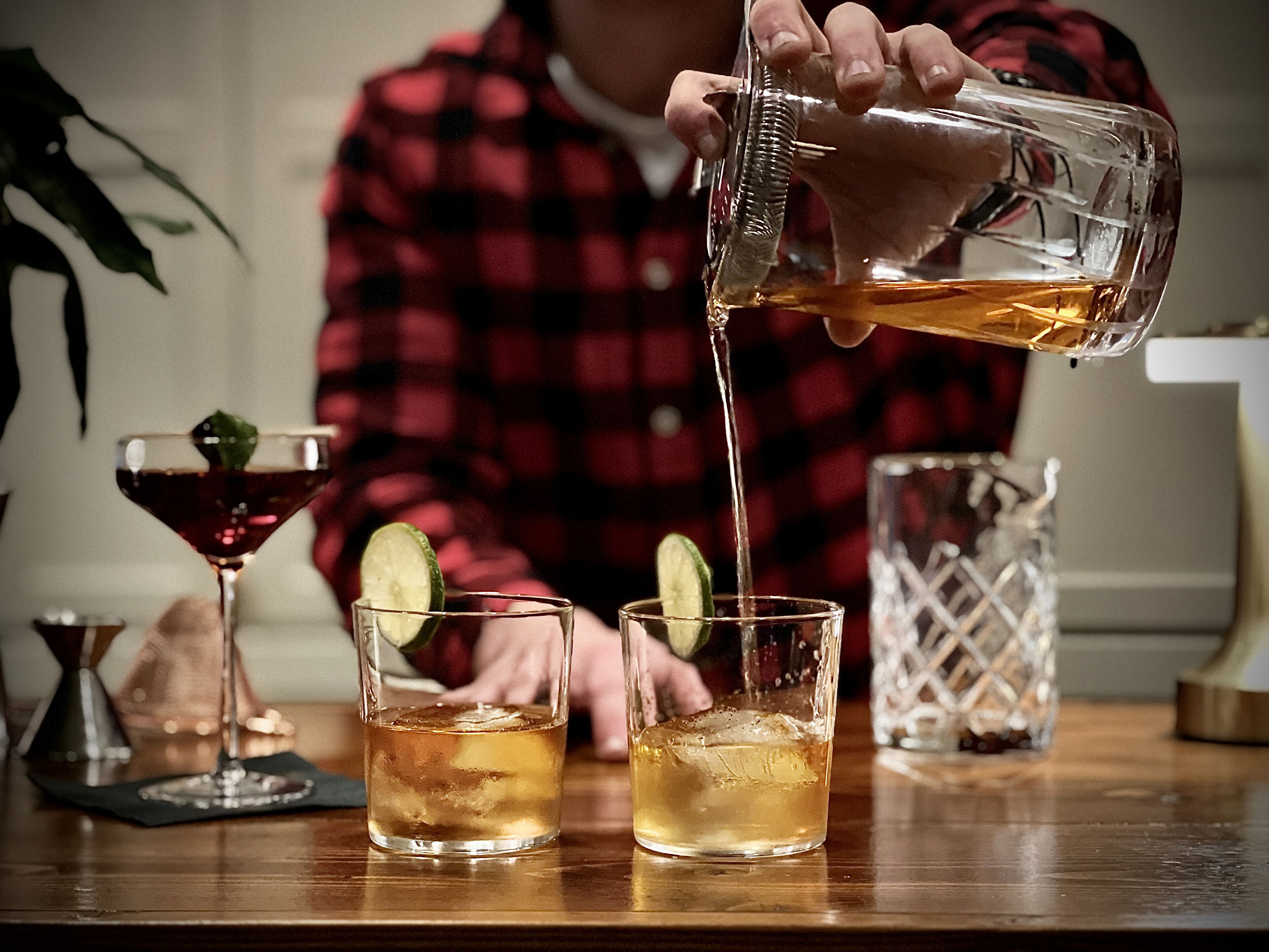 A person pouring a drink into two glasses on a wooden table.