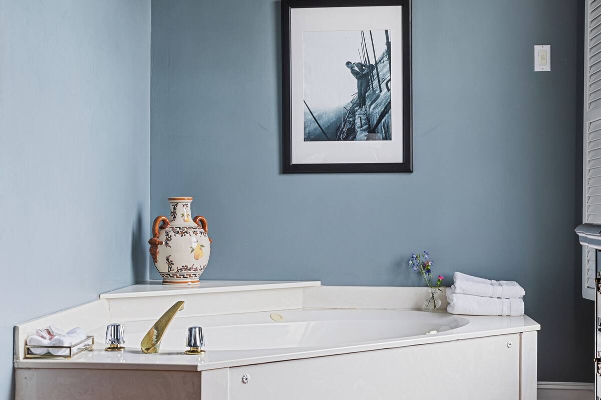 A bathroom with a white vanity, a large vase, a framed picture on the wall, and a wooden floor.
