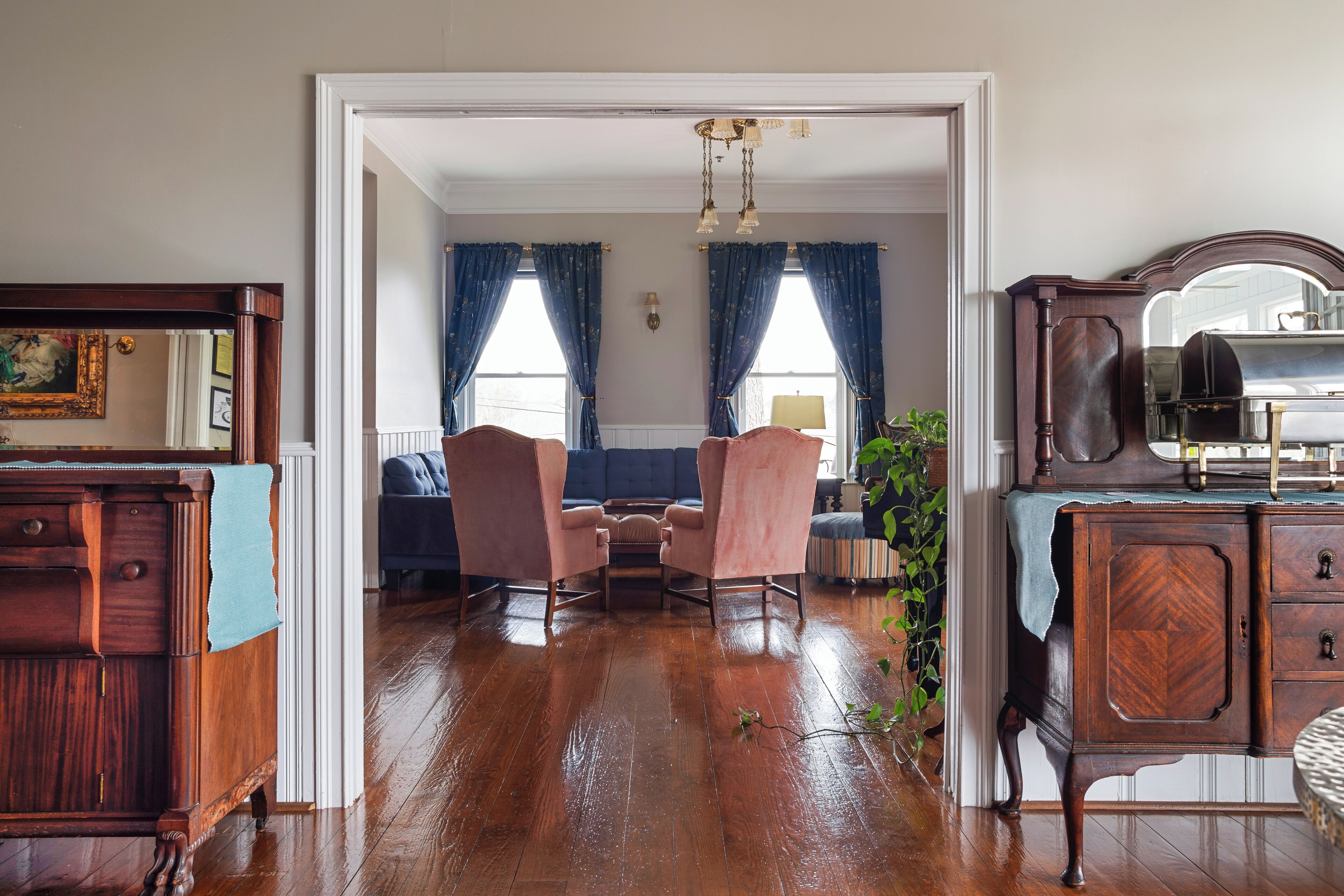 A room with a wooden floor, a blue sofa set, a wooden dresser, and a mirror.