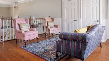 A living room with two pink armchairs, a plaid sofa, a patterned rug, and a wooden staircase.