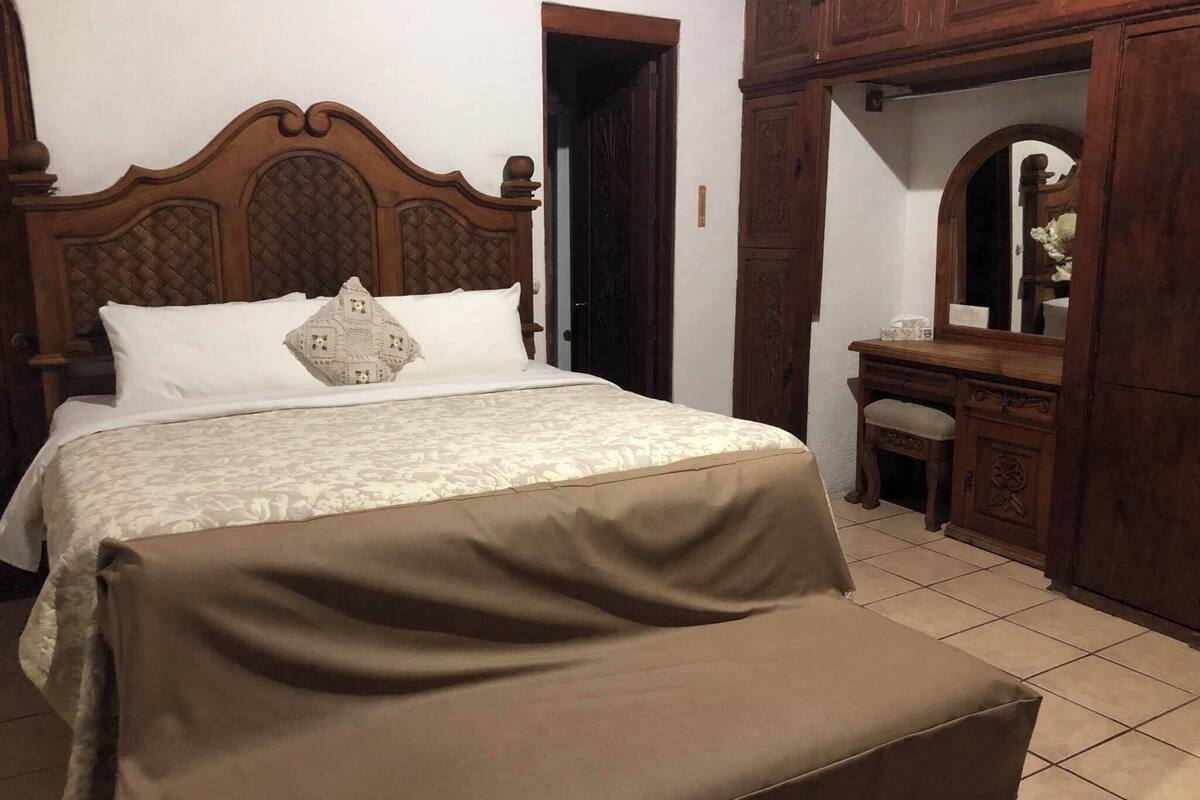 Ein Schlafzimmer mit Bett, Holz-Kopfteil, Nachttisch, Schminktisch und Spiegel.