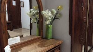 A wooden vanity with a mirror, a green vase with flowers, and a cabinet with a drawer. - Hotel Eden de los Angeles (San Miguel de Allende)