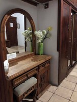 Un tocador de madera con espejo, un jarrón verde con flores y un armario con cajón.