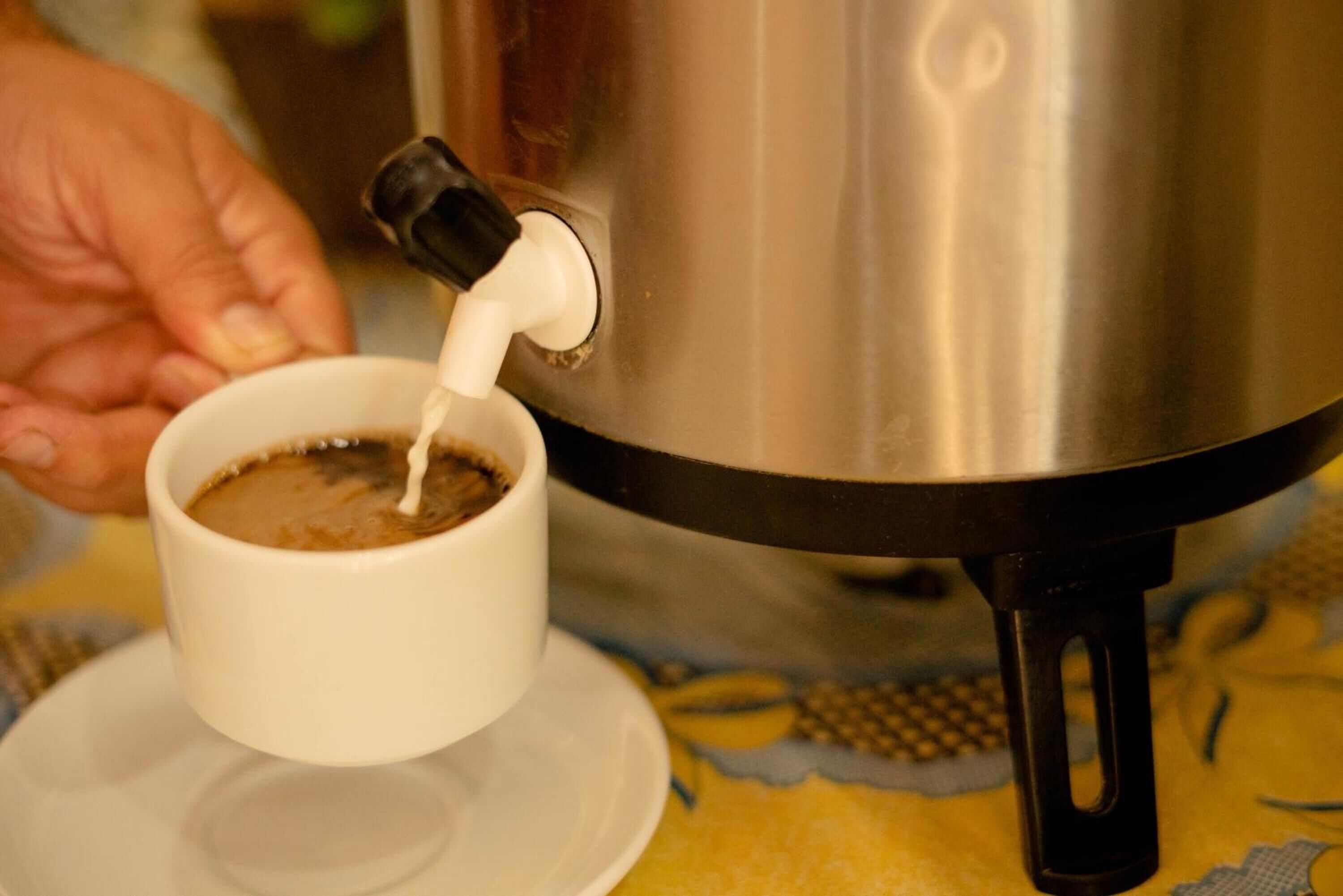 Een hand giet melk in een kop koffie uit een metalen koffiepot.