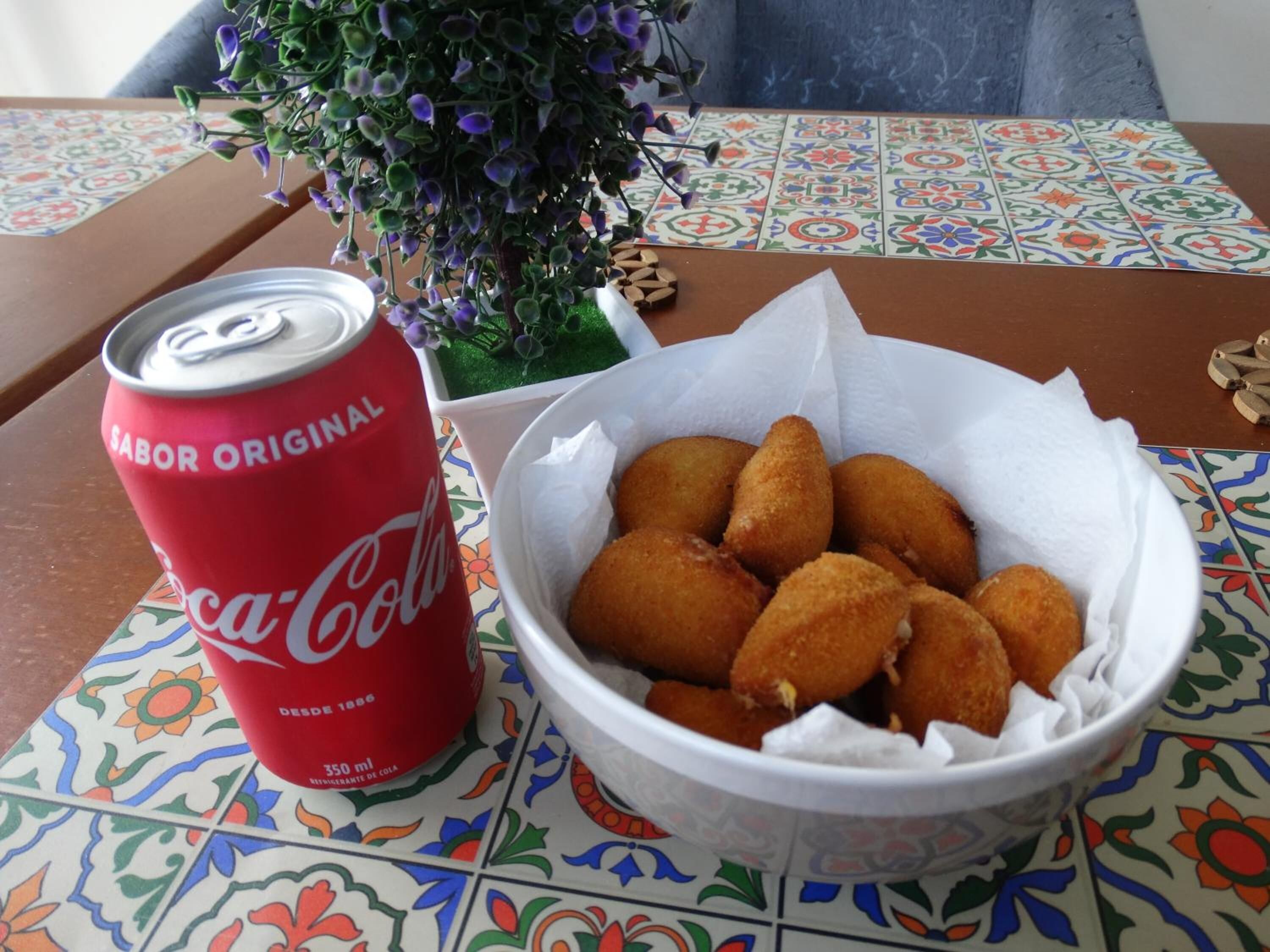 Una mesa con un mantel de mosaicos coloridos, una lata roja de Coca-Cola y un plato de comida frita.