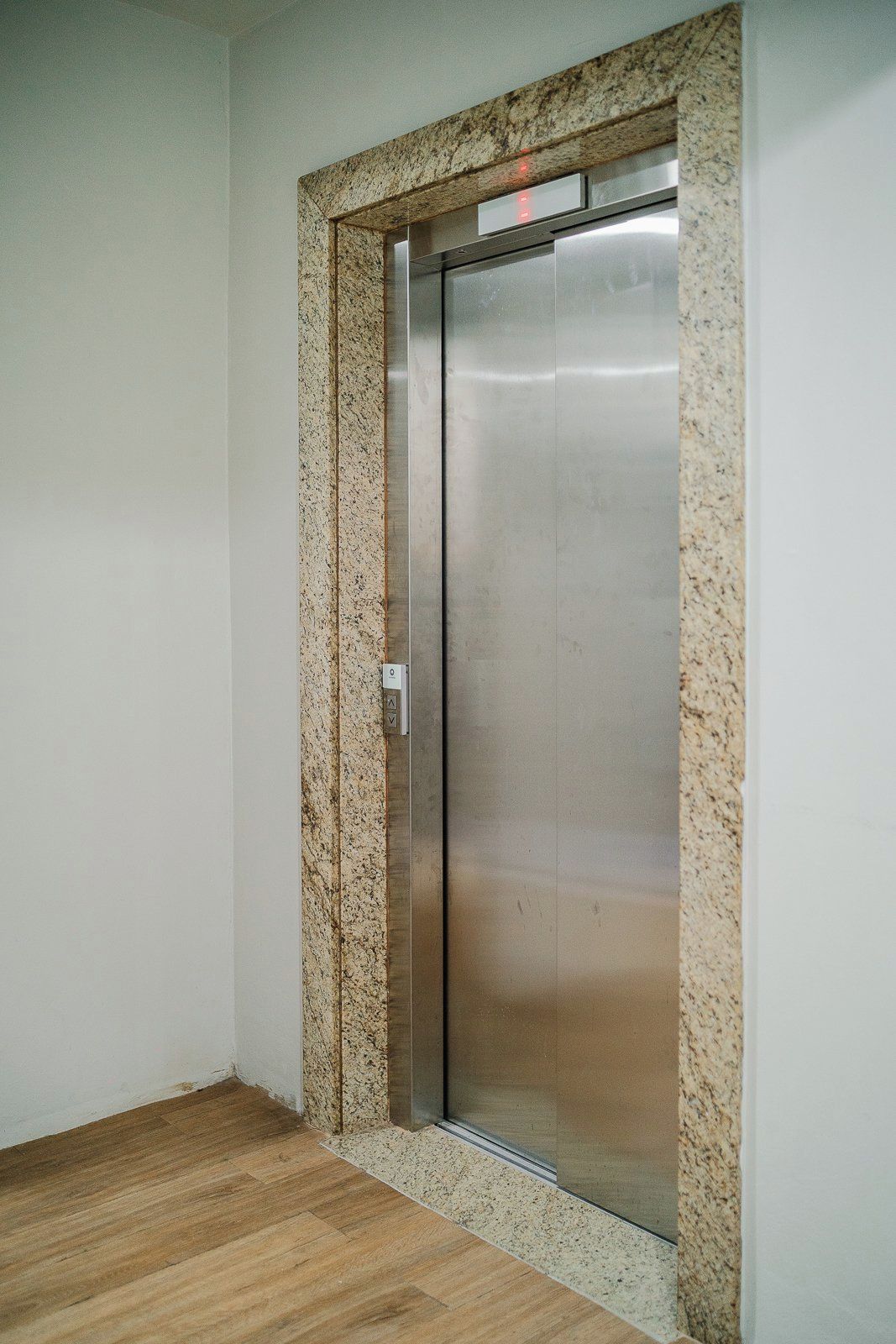 A closed elevator door with a granite frame, a control panel, and a wooden floor.