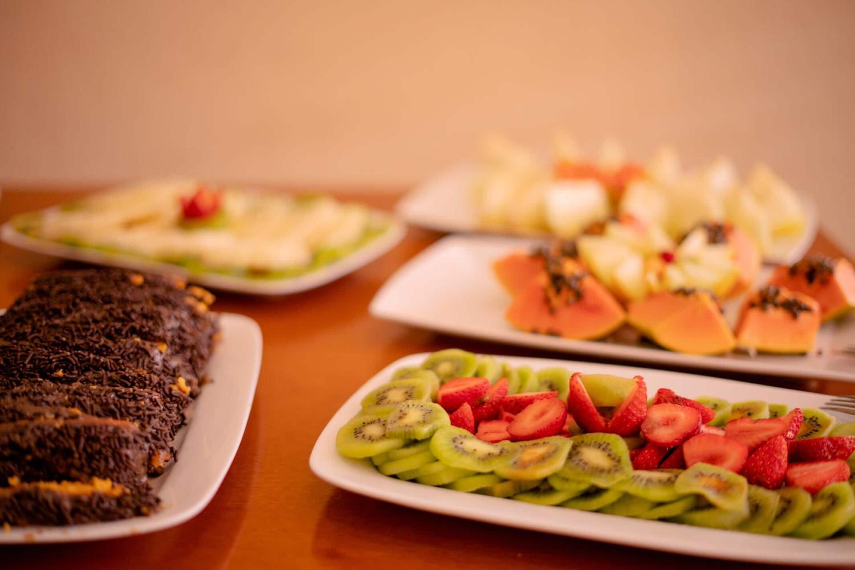 Une table où l’on trouve divers plats, notamment un dessert au chocolat, des tranches de kiwi, des fraises et du melon.